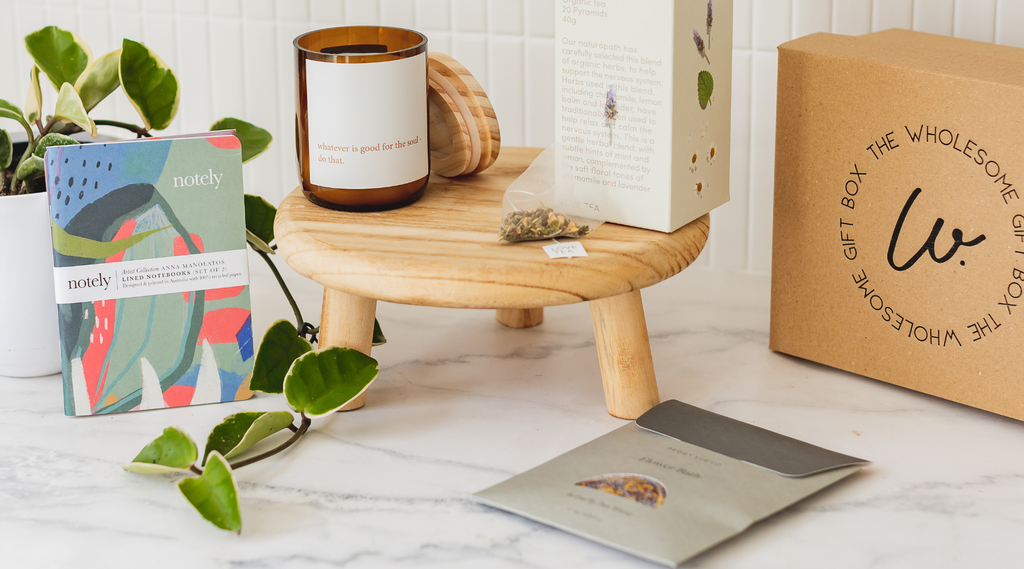 Products included in gift boxes, including: natural soy candle in amber glass jar, organic tea, flower bath, and recycled notebook.